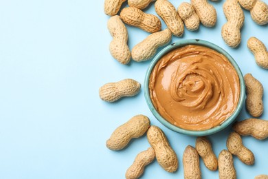 Photo of Tasty peanut butter in bowl and groundnuts on light blue background, flat lay. Space for text