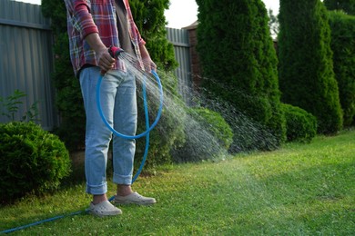 Photo of Man watering green grass on lawn in backyard, closeup