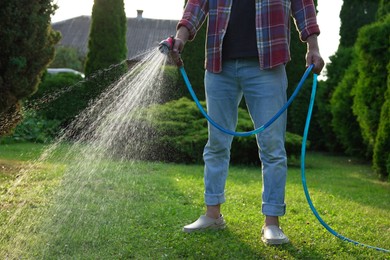 Man watering green grass on lawn in backyard, closeup