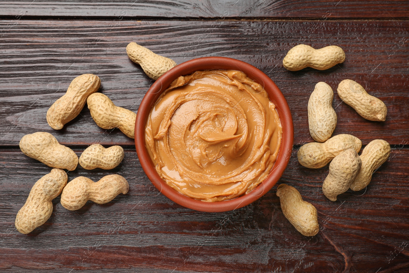 Photo of Tasty peanut butter in bowl and nuts on wooden table, flat lay