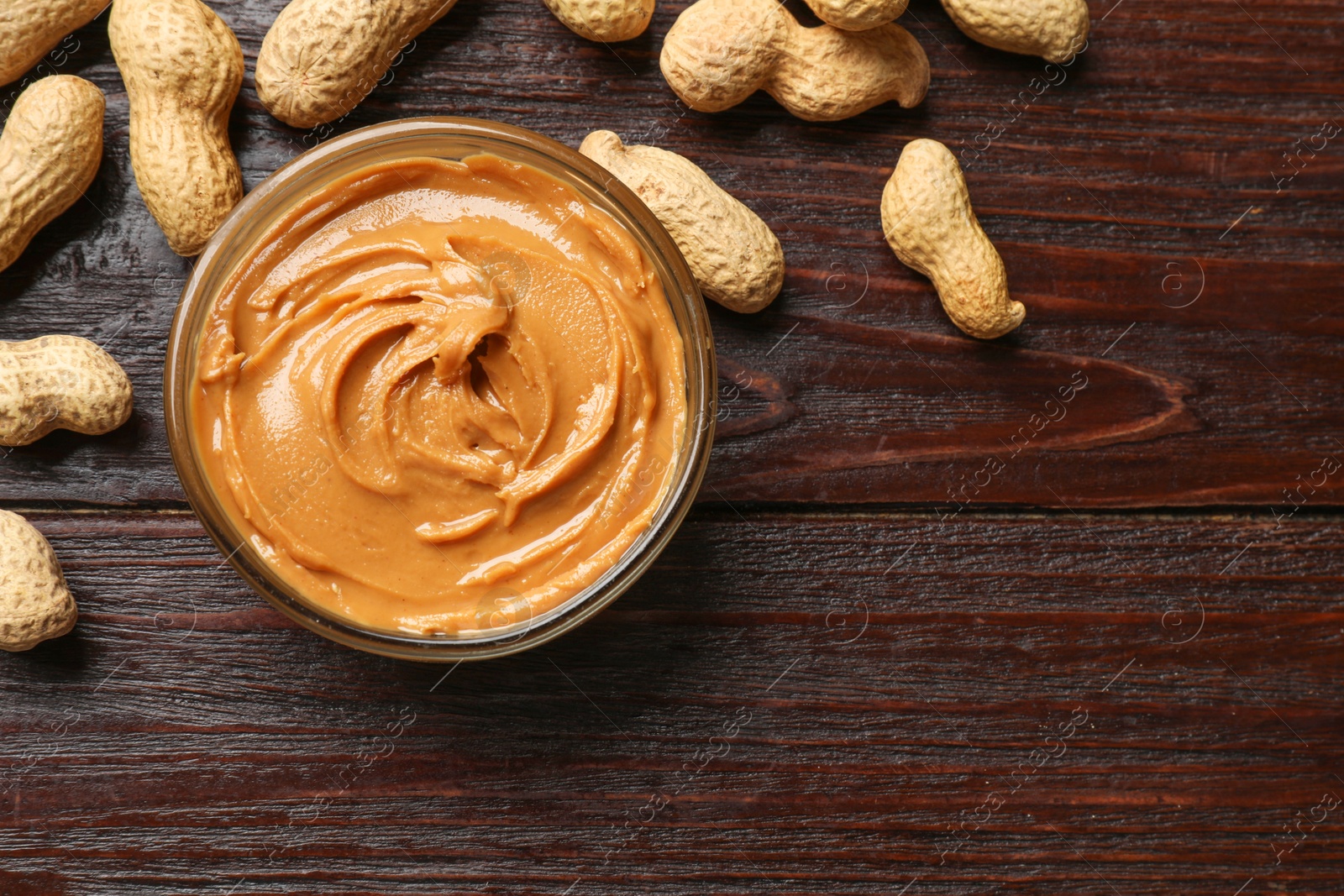 Photo of Tasty peanut butter in bowl and nuts on wooden table, flat lay. Space for text