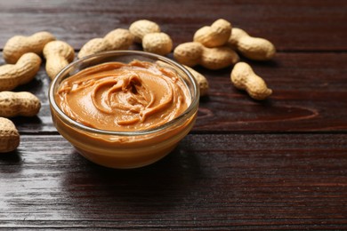 Photo of Tasty peanut butter in bowl and groundnuts on wooden table