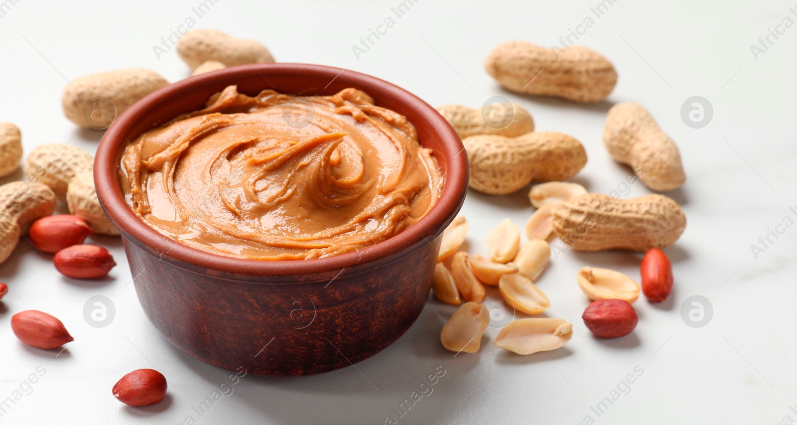 Photo of Tasty peanut butter in bowl and groundnuts on white table, closeup