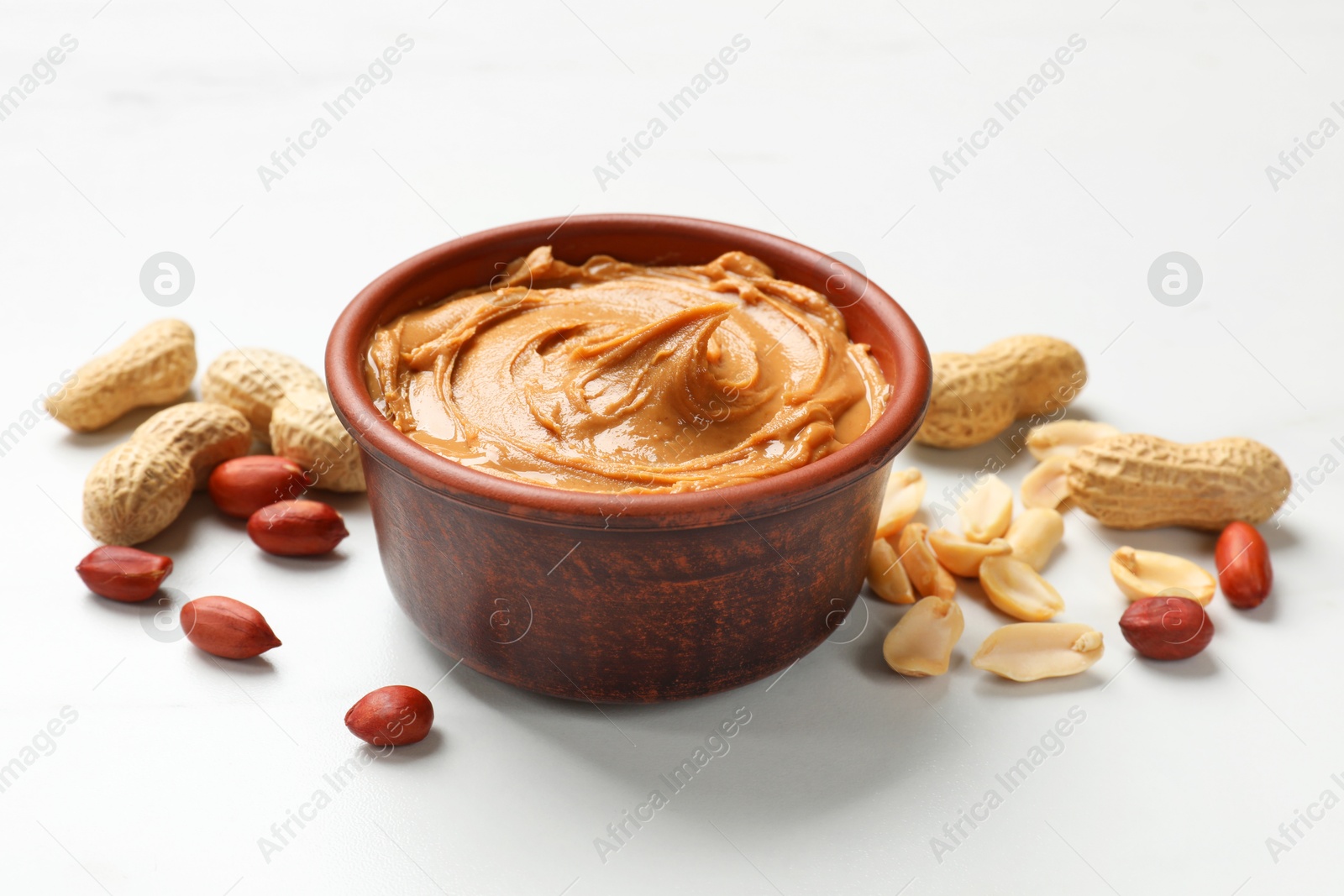 Photo of Tasty peanut butter in bowl and groundnuts on white table