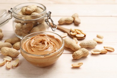 Photo of Tasty peanut butter in bowl, groundnuts, jar and spoon on wooden table, closeup