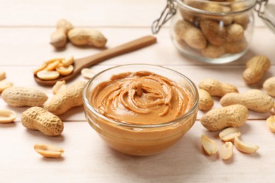 Photo of Tasty peanut butter in bowl, groundnuts, jar and spoon on wooden table, closeup