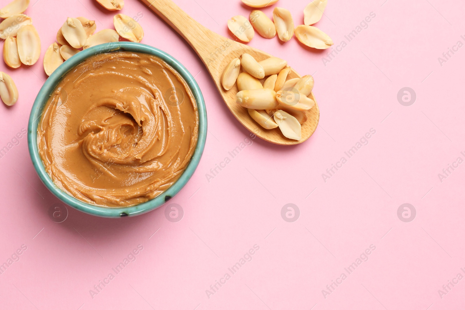 Photo of Tasty peanut butter in bowl and spoon with groundnuts on pink table, flat lay. Space for text