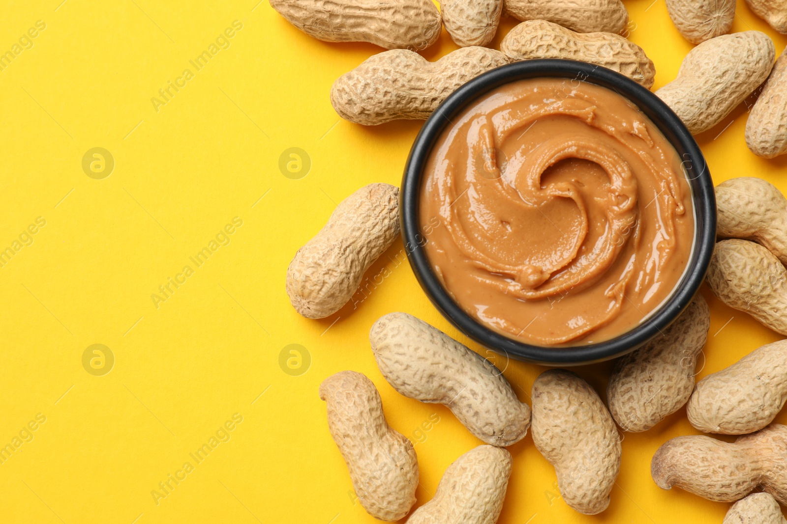 Photo of Tasty peanut butter in bowl and groundnuts on yellow table, flat lay. Space for text