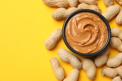 Photo of Tasty peanut butter in bowl and groundnuts on yellow table, flat lay. Space for text