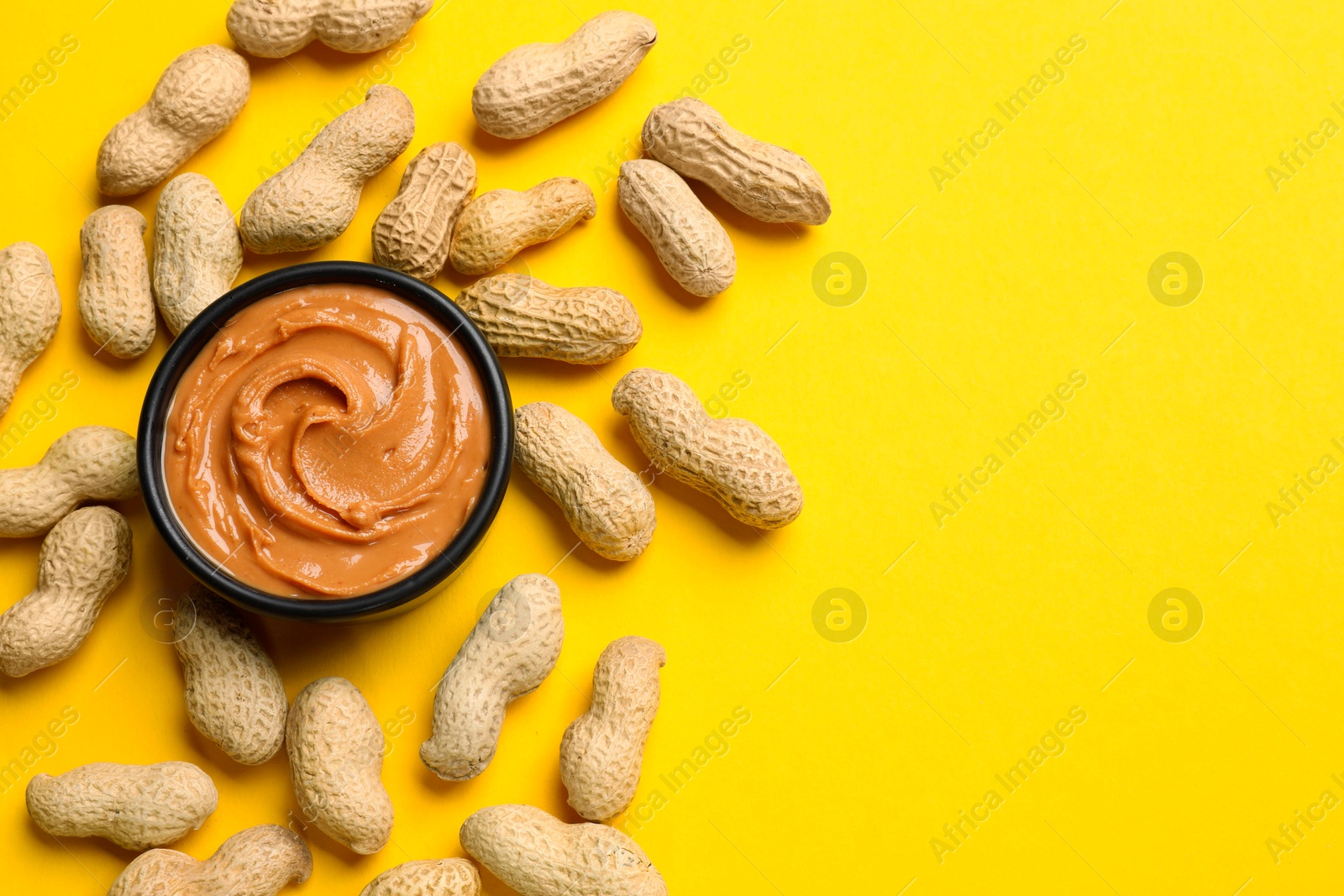 Photo of Tasty peanut butter in bowl and groundnuts on yellow table, flat lay. Space for text