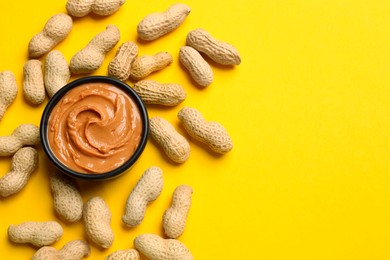 Photo of Tasty peanut butter in bowl and groundnuts on yellow table, flat lay. Space for text