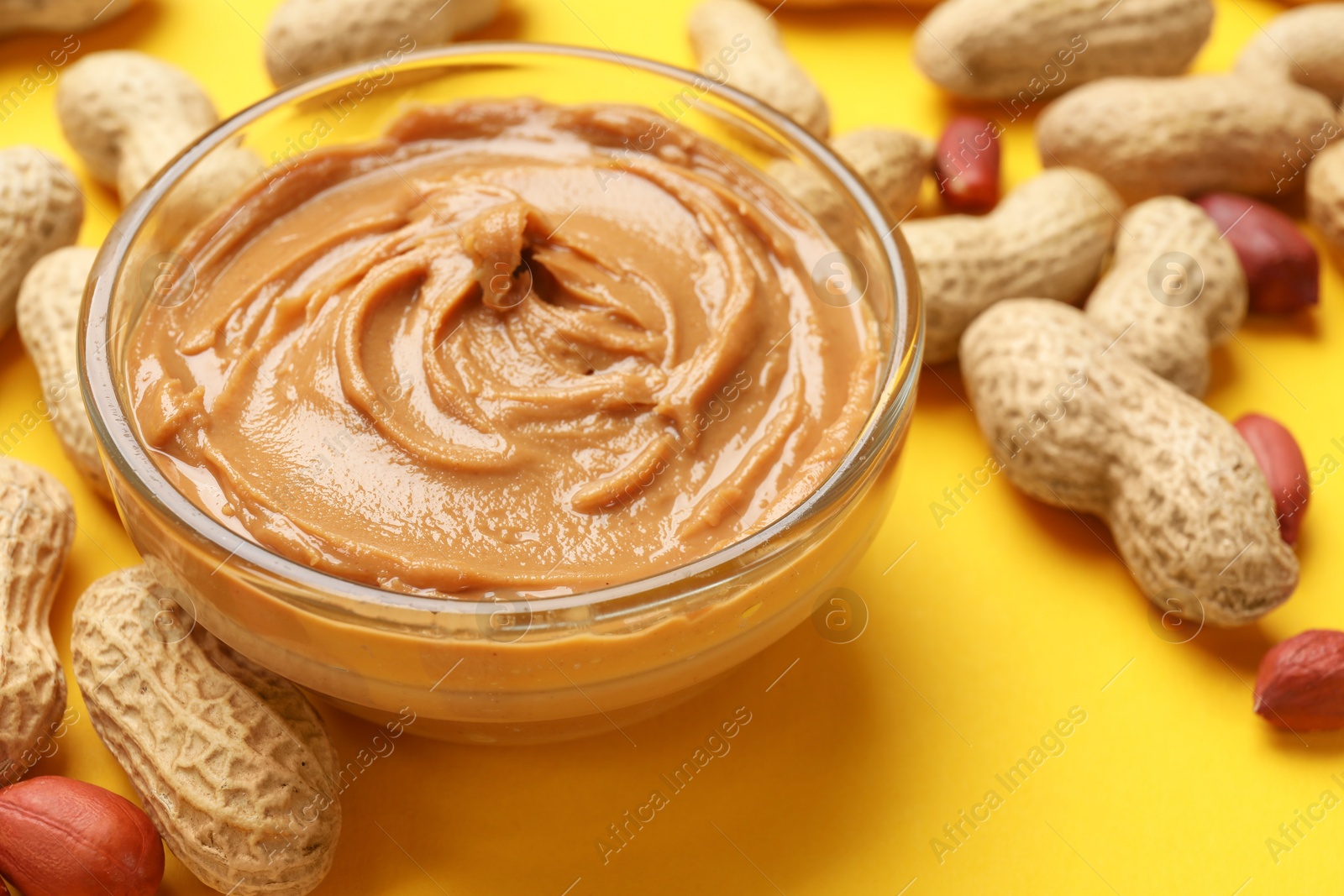 Photo of Tasty peanut butter in bowl and groundnuts on yellow table, closeup