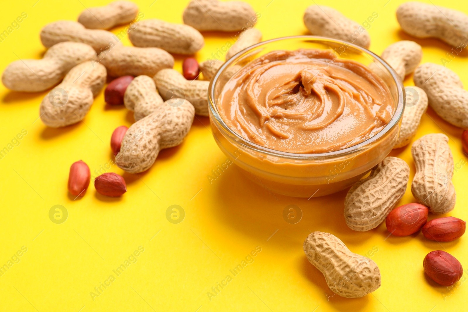 Photo of Tasty peanut butter in bowl and groundnuts on yellow table, closeup