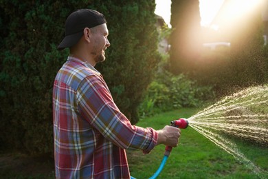 Photo of Man watering lawn with hose in backyard