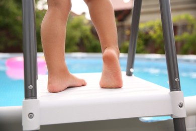 Photo of Little girl on swimming pool ladder outdoors, closeup