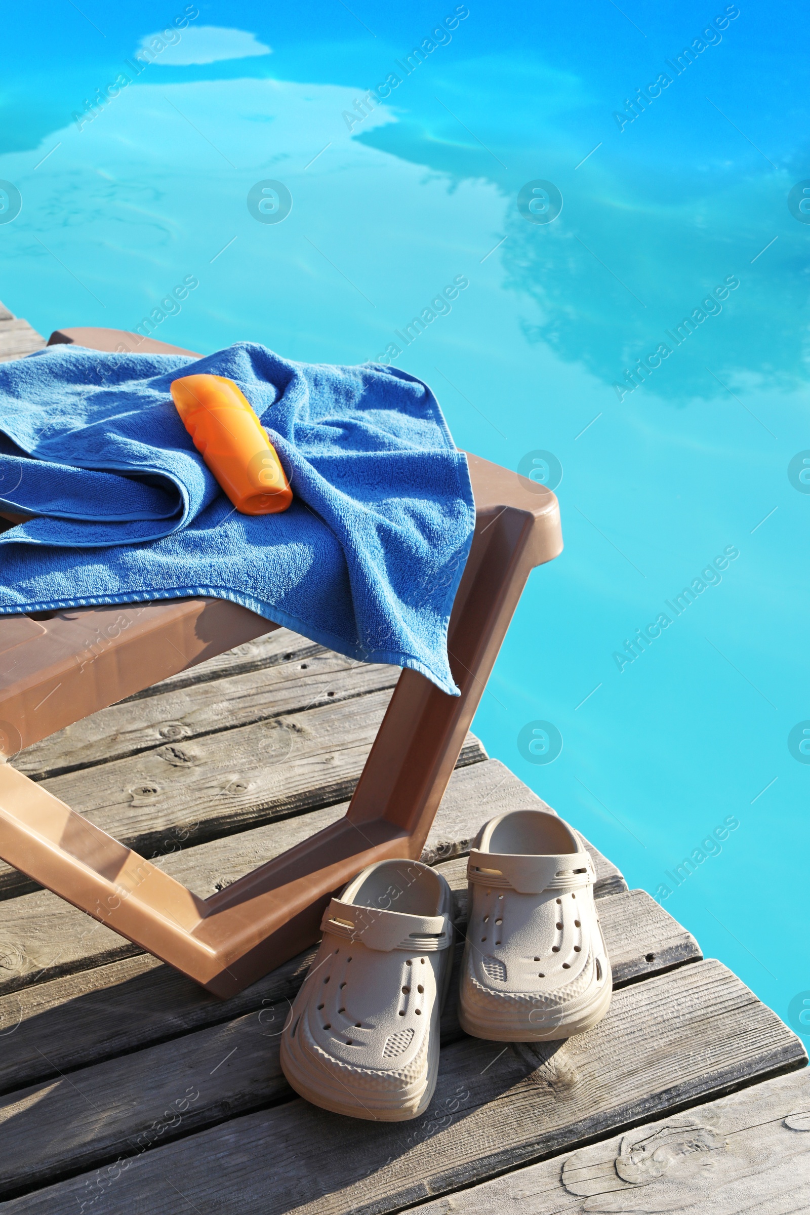 Photo of Beach accessories and sun lounger on wooden deck near outdoor swimming pool