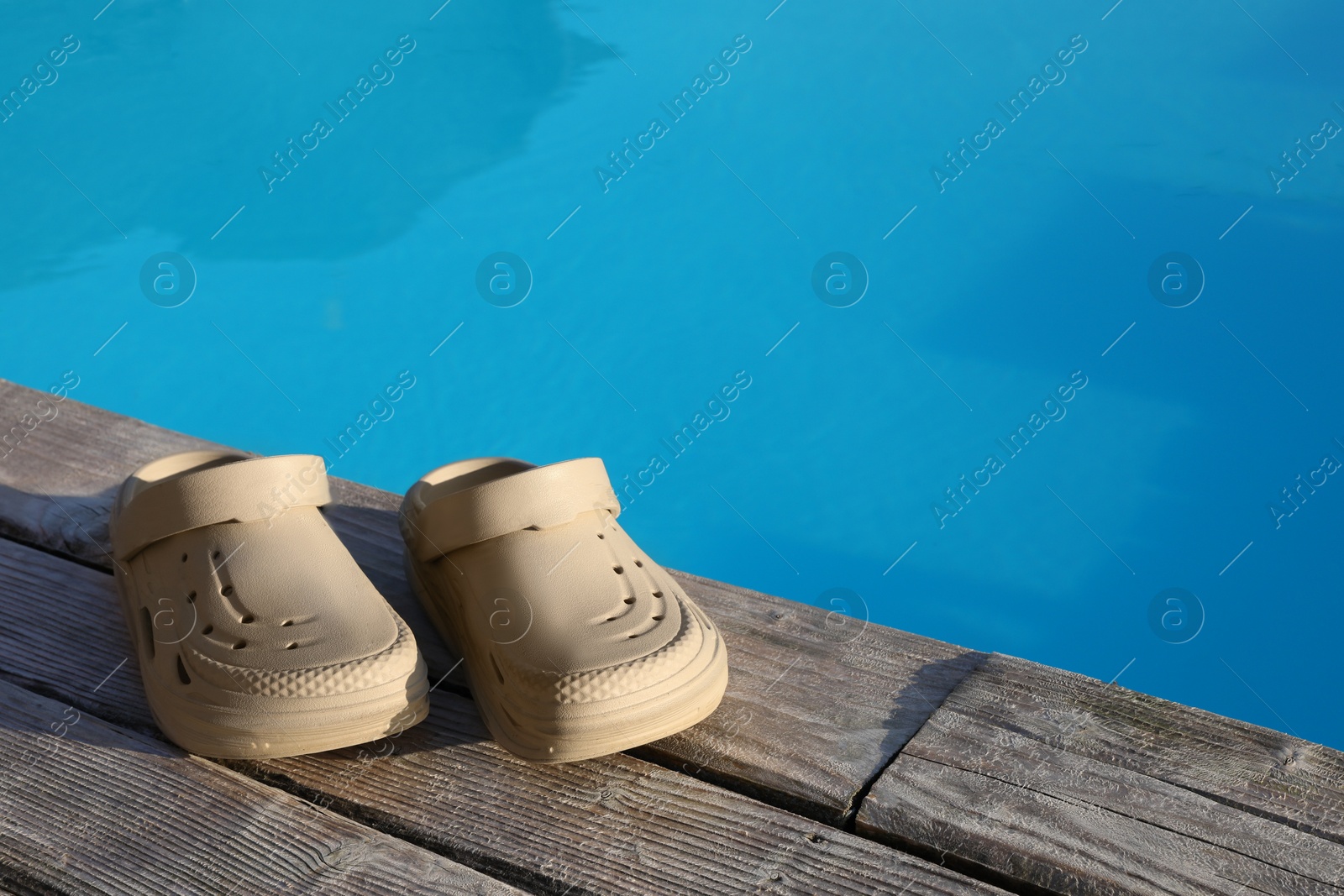 Photo of Stylish beach slippers on wooden deck near outdoor swimming pool