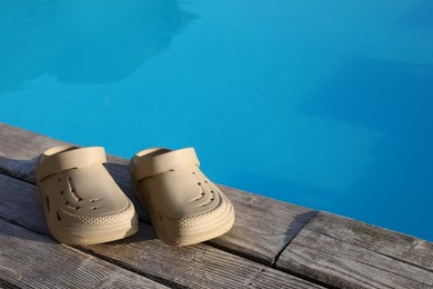 Photo of Stylish beach slippers on wooden deck near outdoor swimming pool