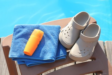 Photo of Stylish beach slippers, towel and sunscreen on sun lounger near outdoor swimming pool