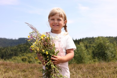 Photo of Smiling little girl with bouquet of wildflowers at field