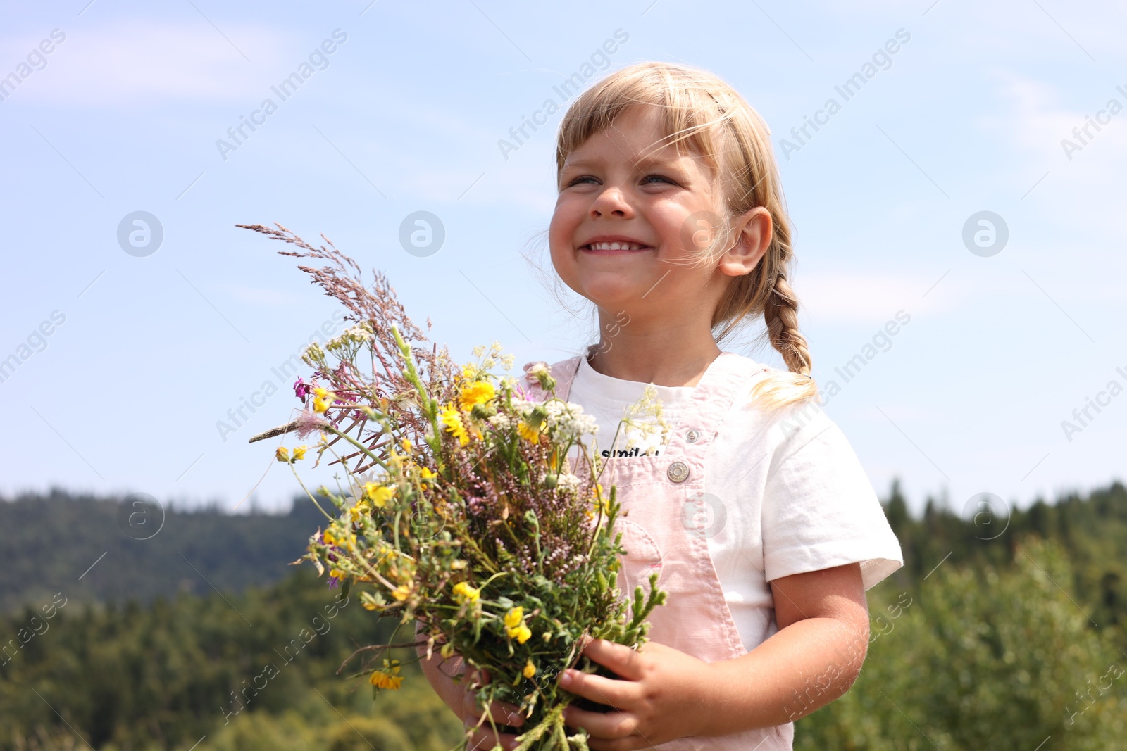 Photo of Smiling little girl with bouquet of wildflowers at field