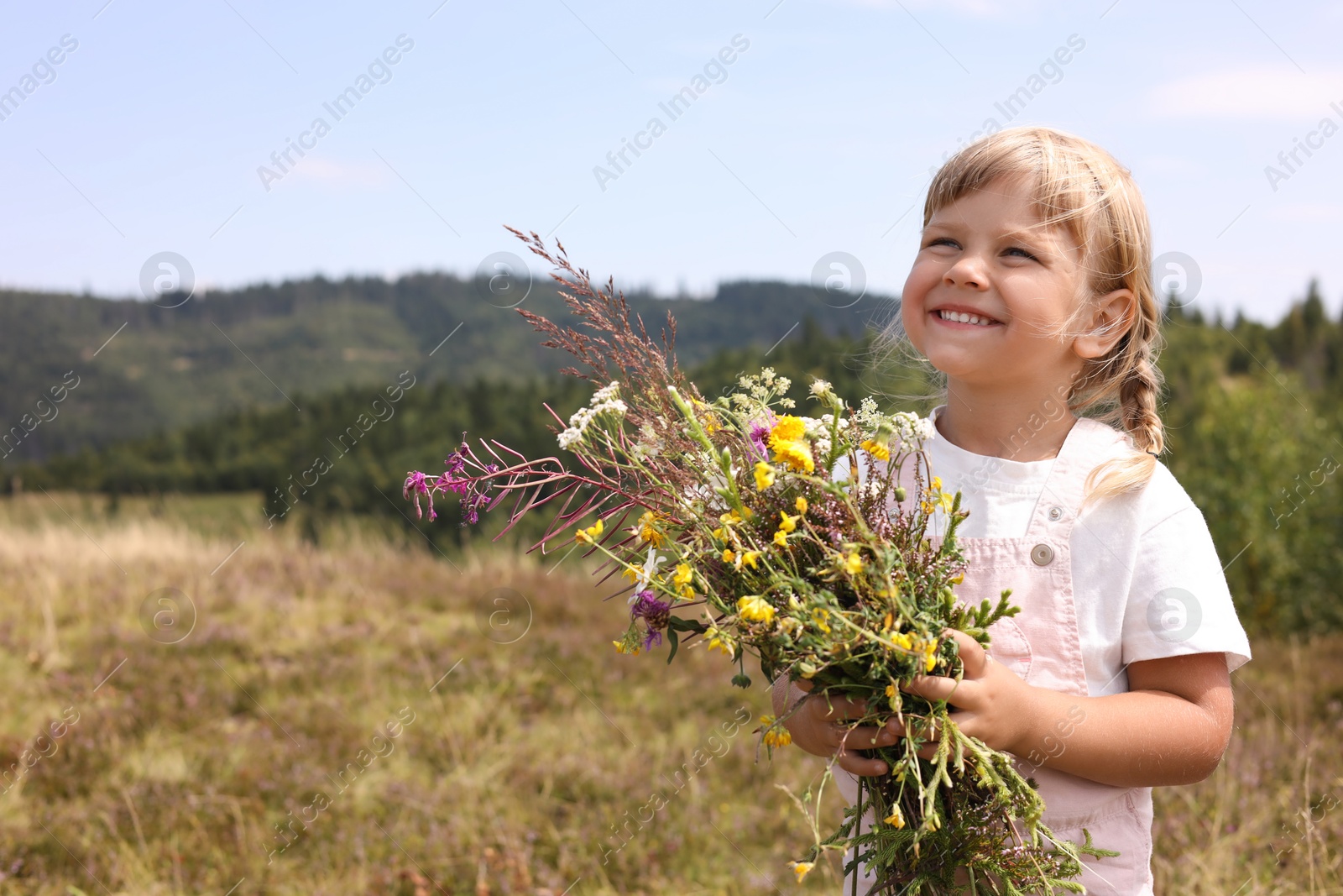 Photo of Smiling little girl with bouquet of wildflowers at field, space for text