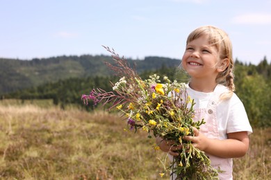 Photo of Smiling little girl with bouquet of wildflowers at field, space for text