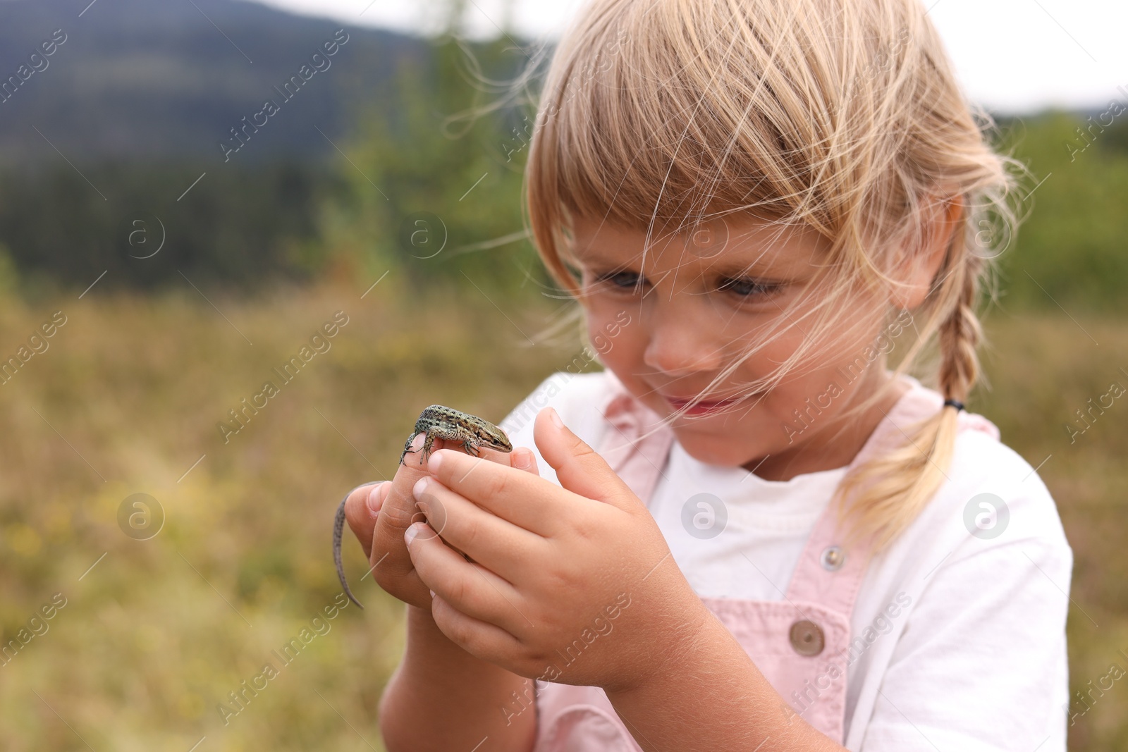 Photo of Happy little girl holding small lizard outdoors