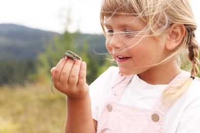 Happy little girl holding small lizard outdoors