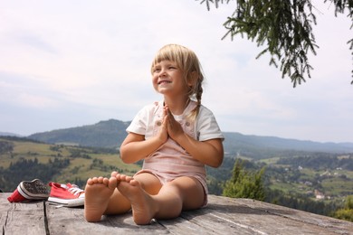 Photo of Cute little girl sitting on wooden deck in mountains