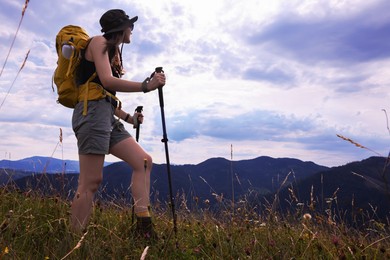 Photo of Young hiker with backpack and trekking poles in mountains, space for text