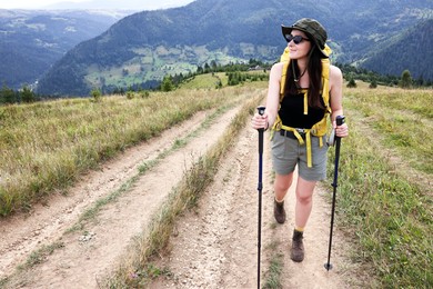 Young hiker with backpack and trekking poles in mountains, space for text