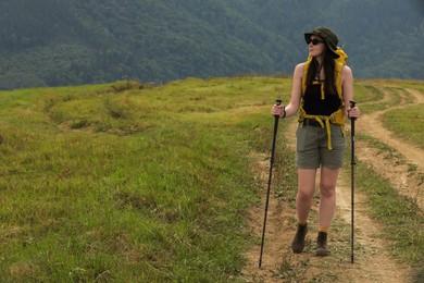 Photo of Young hiker with backpack and trekking poles in mountains, space for text