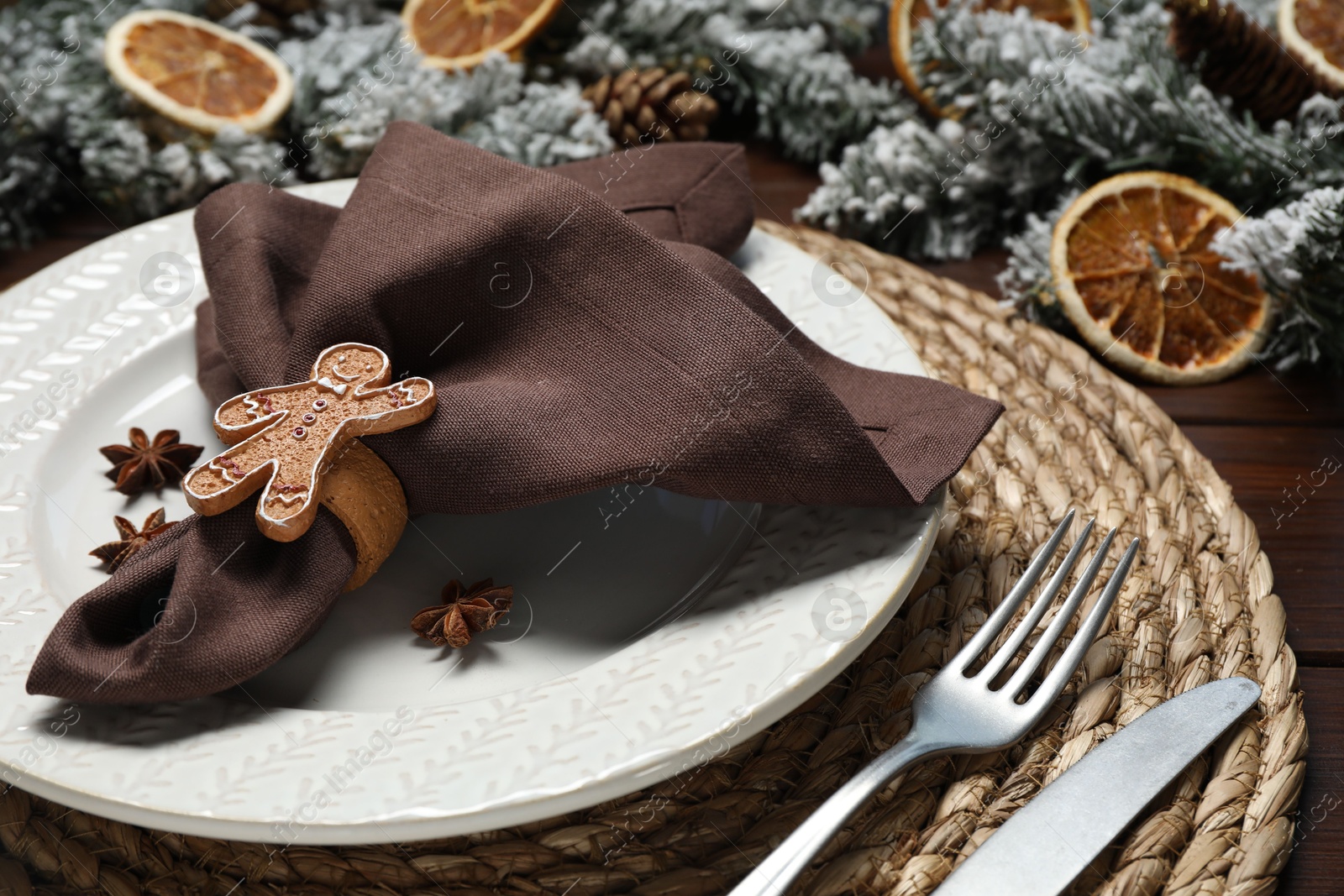 Photo of Christmas place setting with napkin, plate, cutlery and festive decor on wooden table, closeup