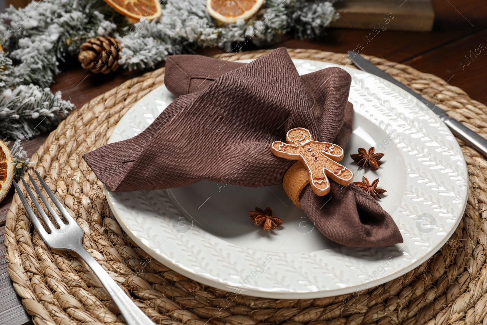 Photo of Christmas place setting with napkin, plate, cutlery and festive decor on wooden table, closeup