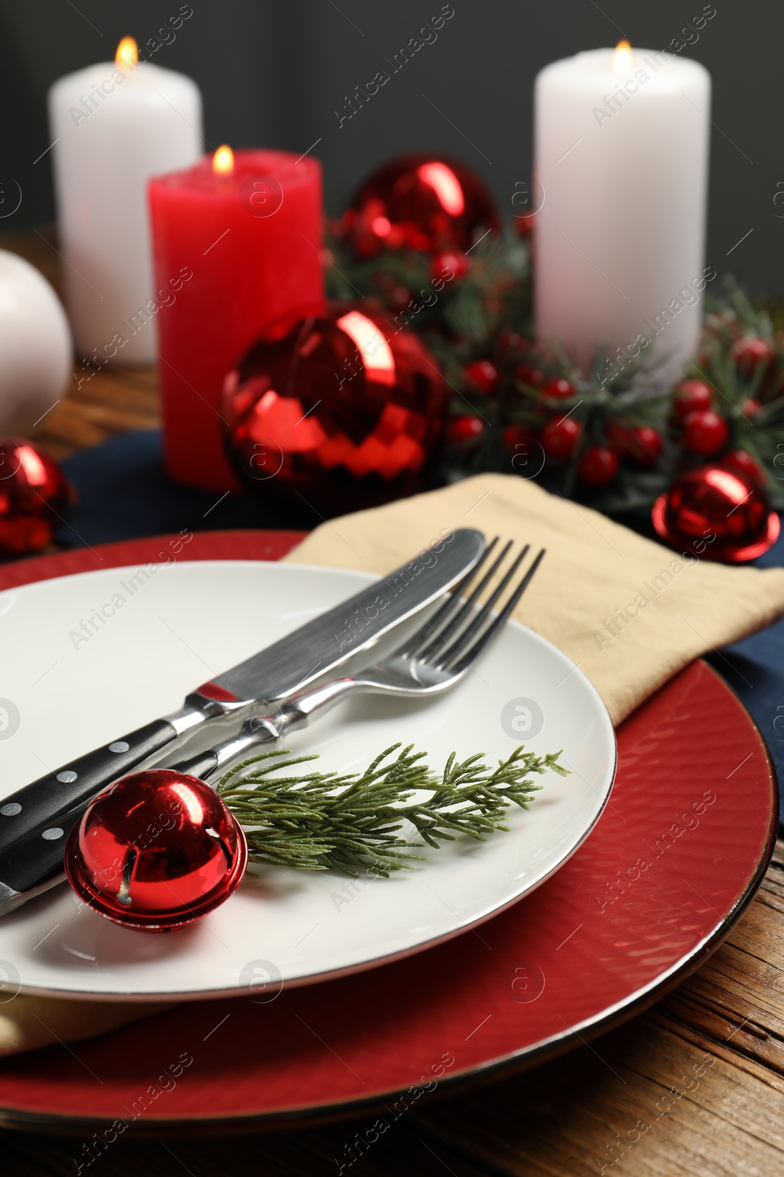 Photo of Christmas place setting with plates, cutlery and festive decor on wooden table, closeup