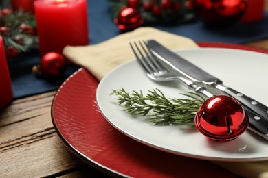 Photo of Christmas place setting with plates, cutlery and festive decor on wooden table, closeup