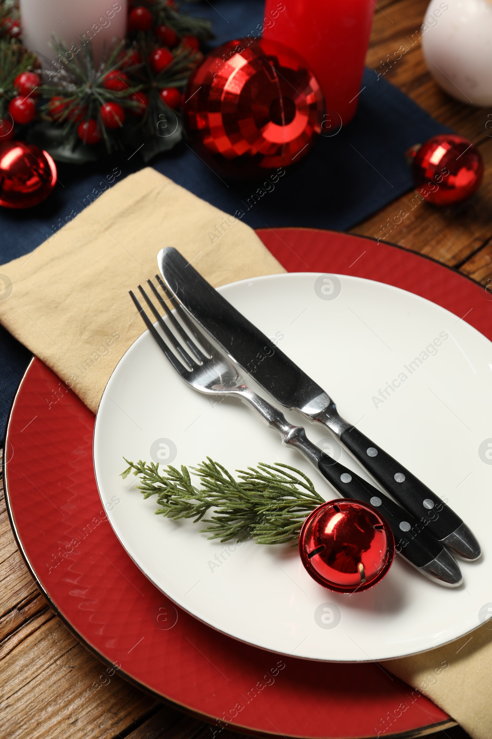 Photo of Christmas place setting with plates, cutlery and festive decor on wooden table, closeup