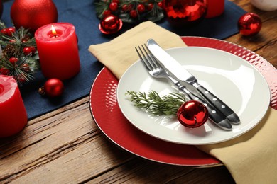 Photo of Christmas place setting with plates, cutlery and festive decor on wooden table, closeup