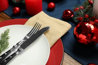 Photo of Christmas place setting with plates, cutlery and festive decor on wooden table, closeup