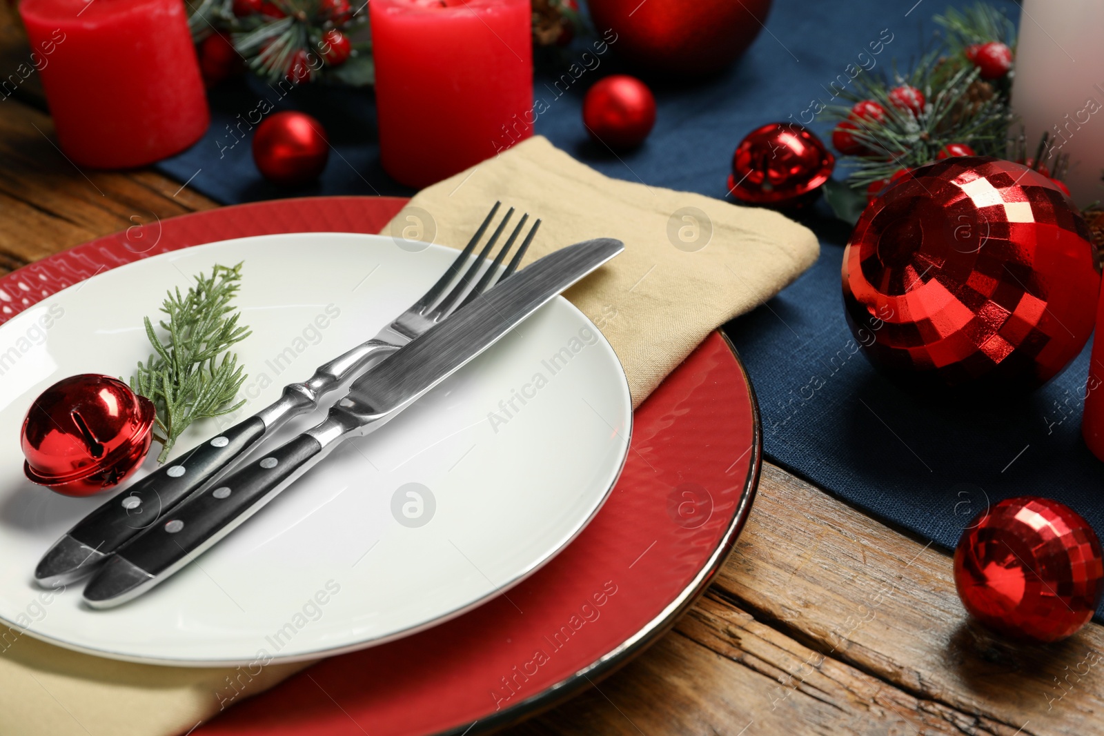 Photo of Christmas place setting with plates, cutlery and festive decor on wooden table, closeup