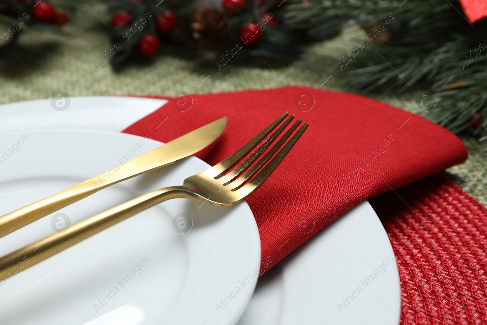 Photo of Christmas place setting with plates, cutlery and festive decor on green tablecloth, closeup