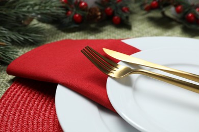 Photo of Christmas place setting with plates, cutlery and festive decor on green tablecloth, closeup