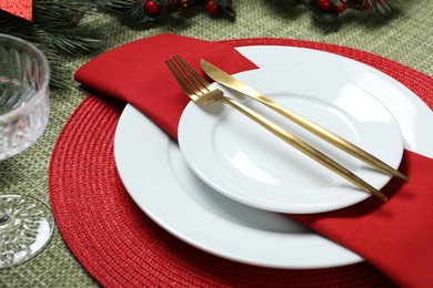 Photo of Christmas place setting with plates, cutlery and festive decor on green tablecloth, closeup