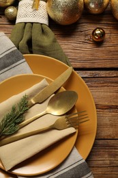 Photo of Christmas place setting with plates, cutlery and festive decor on wooden table, flat lay