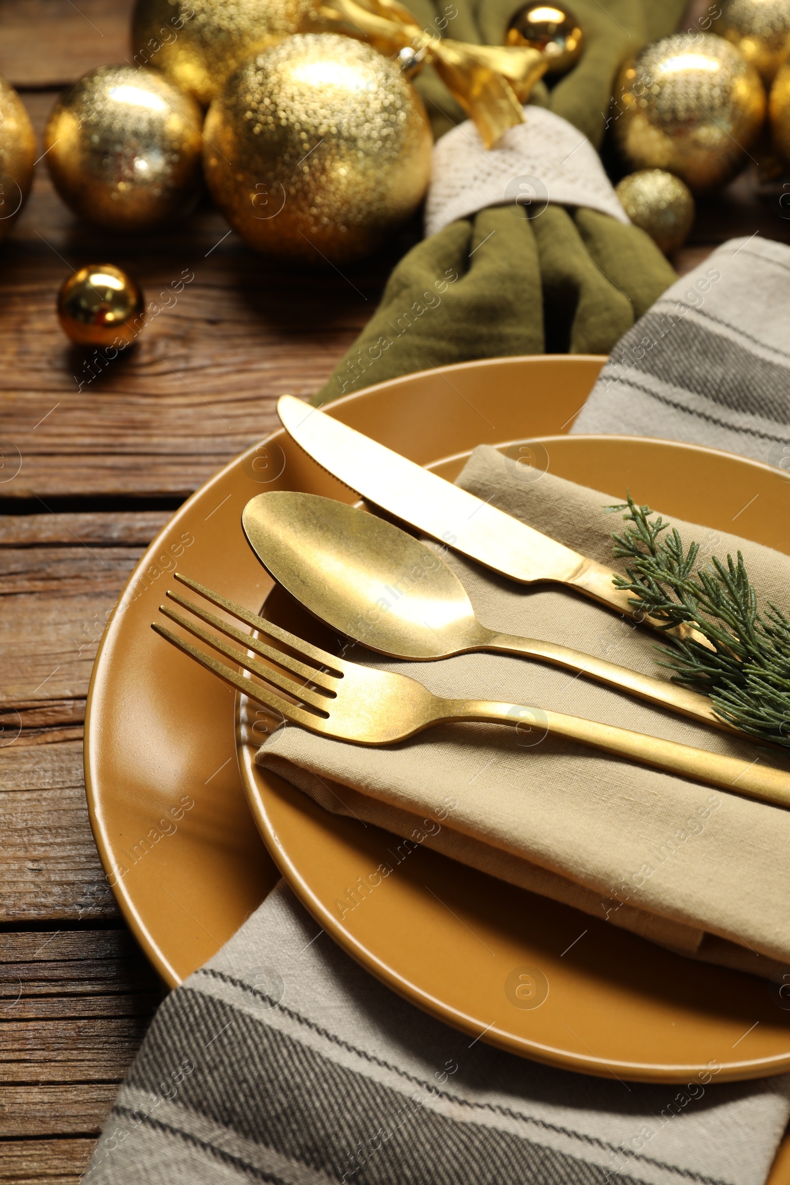 Photo of Christmas place setting with plates, cutlery and festive decor on wooden table, closeup