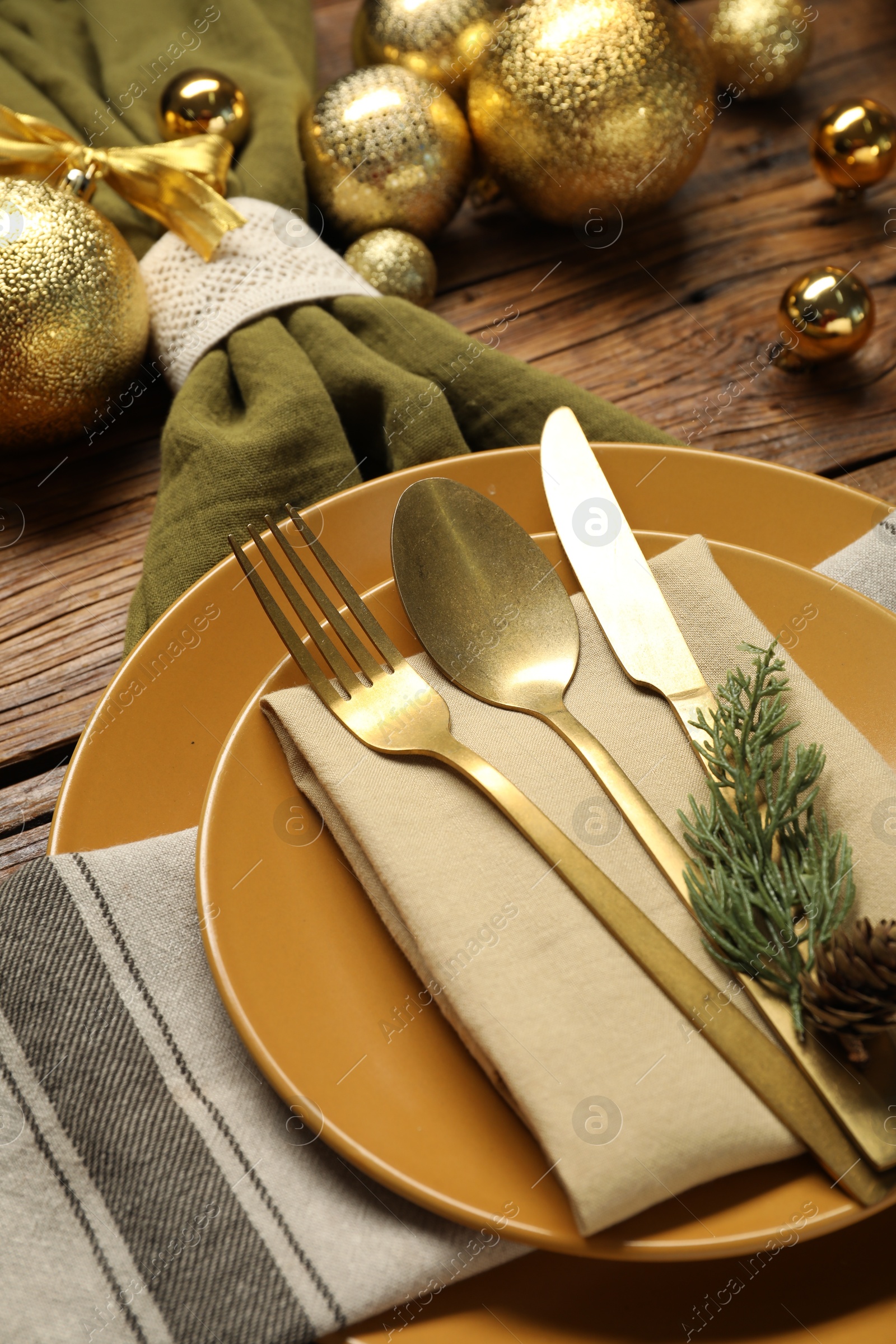 Photo of Christmas place setting with plates, cutlery and festive decor on wooden table, closeup