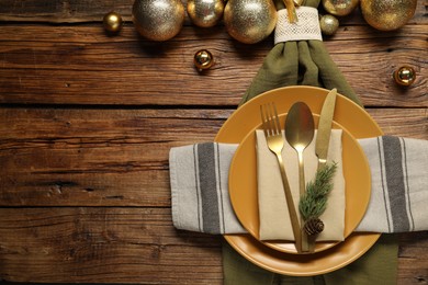 Photo of Christmas place setting with plates, cutlery and festive decor on wooden table, flat lay. Space for text