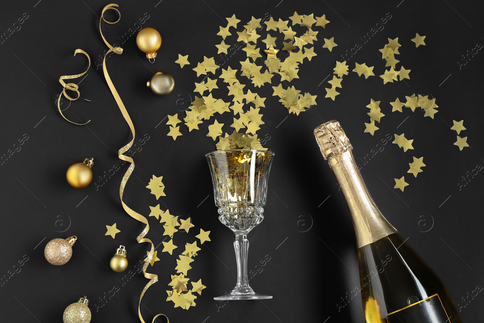 Photo of Flat lay composition with Christmas balls, confetti and bottle of sparkling wine on black background