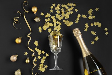 Photo of Flat lay composition with Christmas balls, confetti and bottle of sparkling wine on black background